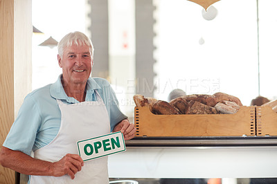 Buy stock photo Portrait of a happy senior man holding up an open sign in his bakery