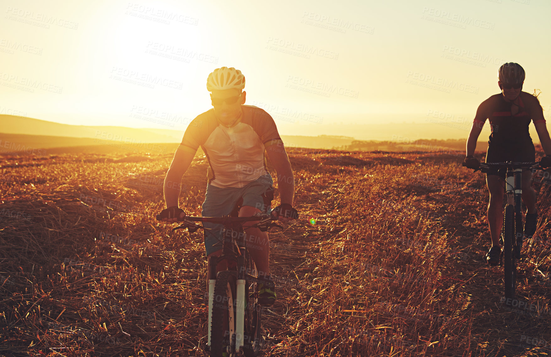 Buy stock photo Sunset, path and friends in bicycle race with helmet, exercise and adventure trail in nature together. Cycling, fitness and people with mountain bike in evening for outdoor workout, energy and sky