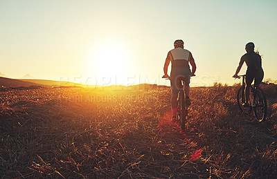 Buy stock photo Sunset sky, people and friends in bicycle race with grass, exercise and adventure trail in nature together. Cycling, fitness and team with mountain bike in evening for outdoor workout, sun and mockup