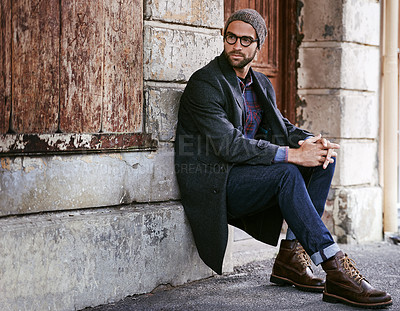 Buy stock photo Shot of a handsome young man taking a seat on the sidewalk in the city
