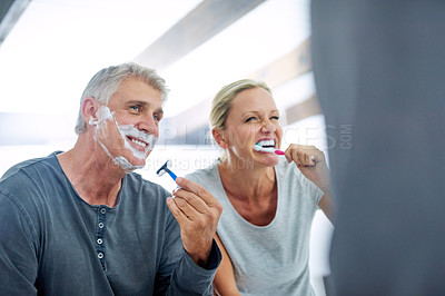 Buy stock photo Cropped shot of a mature man shaving his face while his wife brushes her teeth in the bathroom