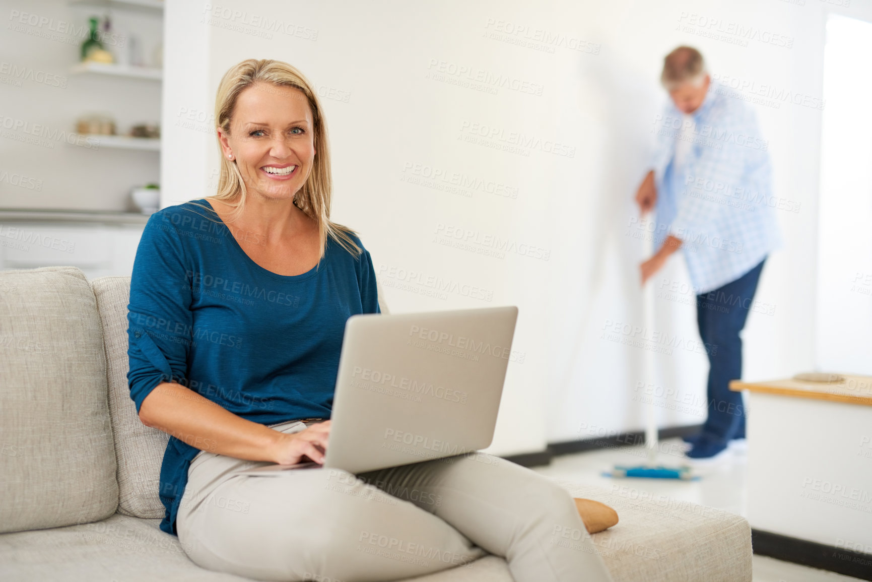 Buy stock photo Mature, woman and house on couch with laptop, browsing and internet search or social media break in living room. Man, sweeping for house maintenance, married couple and weekend together in apartment