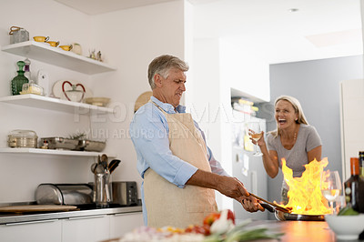 Buy stock photo Shot of a mature man flambéing food while his wife laughs with enjoyment