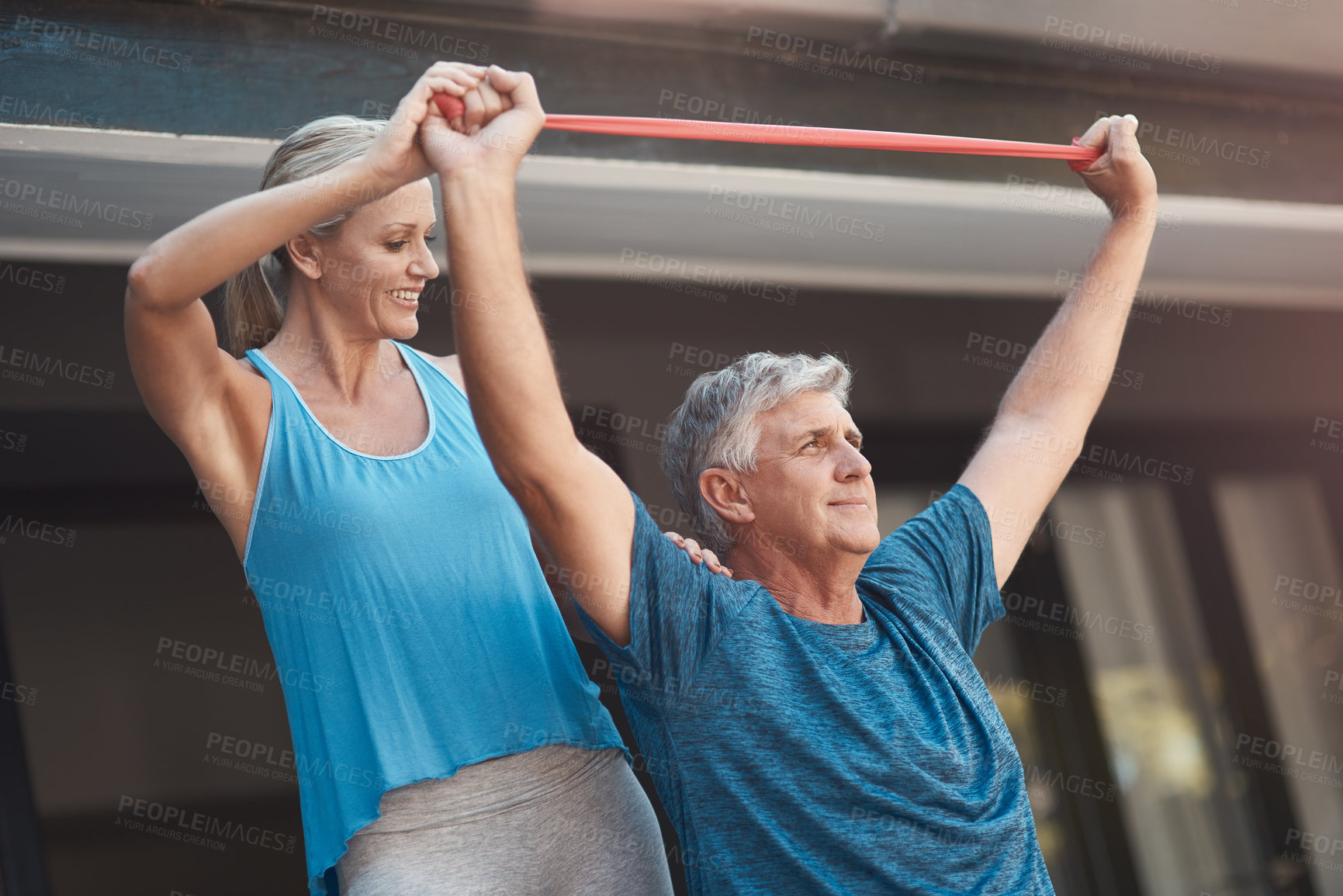 Buy stock photo Shot of a mature man stretching his arm muscles with an elastic band while being assisted by a woman
