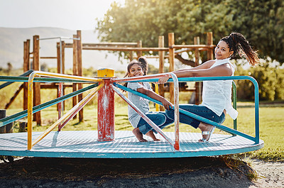 Buy stock photo Portrait of a mother and her daughter playing together on a merry-go-round at the park