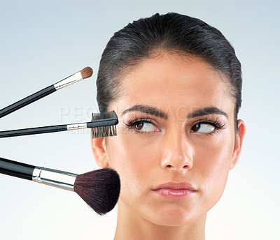 Buy stock photo Studio shot of a beautiful young woman holding makeup brushes and looking annoyed against a gray background