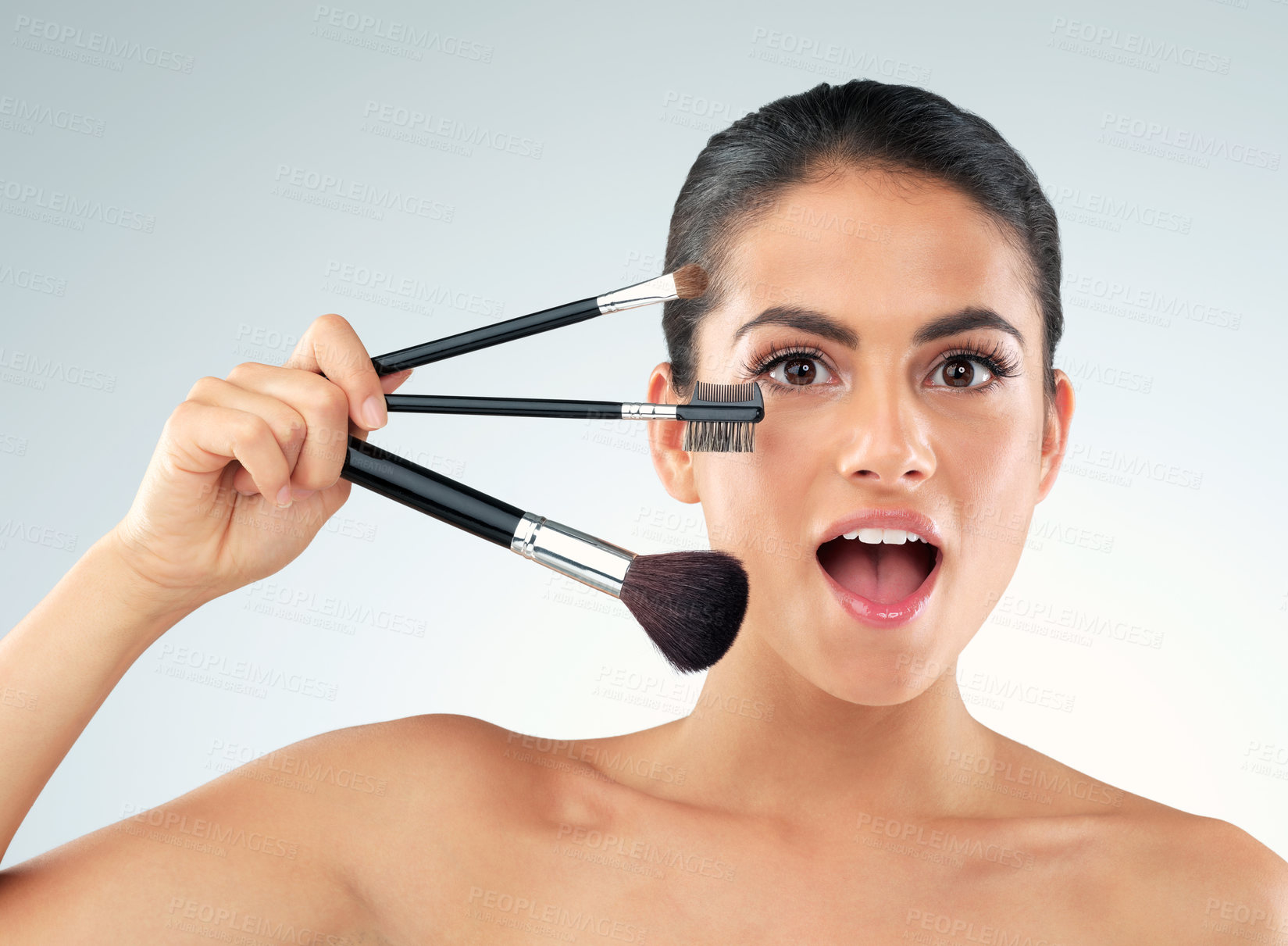 Buy stock photo Studio shot of a beautiful young woman holding makeup brushes against a gray background