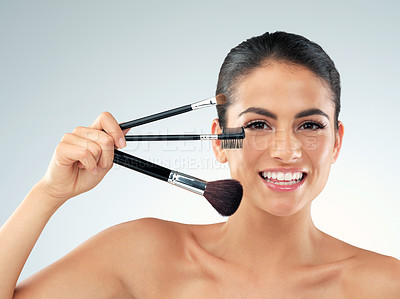 Buy stock photo Studio shot of a beautiful young woman holding makeup brushes against a gray background