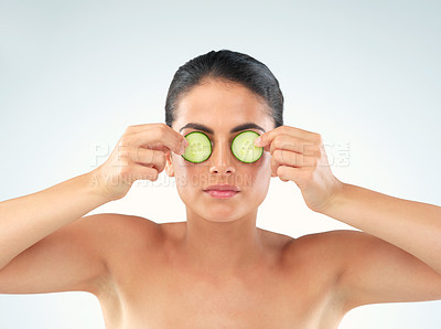 Buy stock photo Studio portrait of a beautiful young woman covering her eyes with cucumbers against a gray background