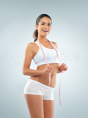Buy stock photo Studio shot of a fit young woman posing with a measuring tape against a gray background