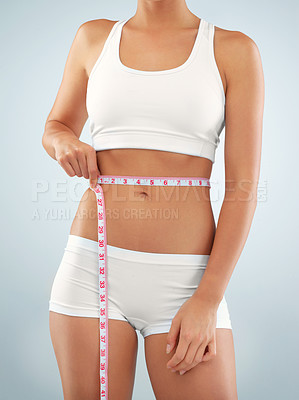 Buy stock photo Cropped studio shot of a fit young woman measuring her waistline against a gray background