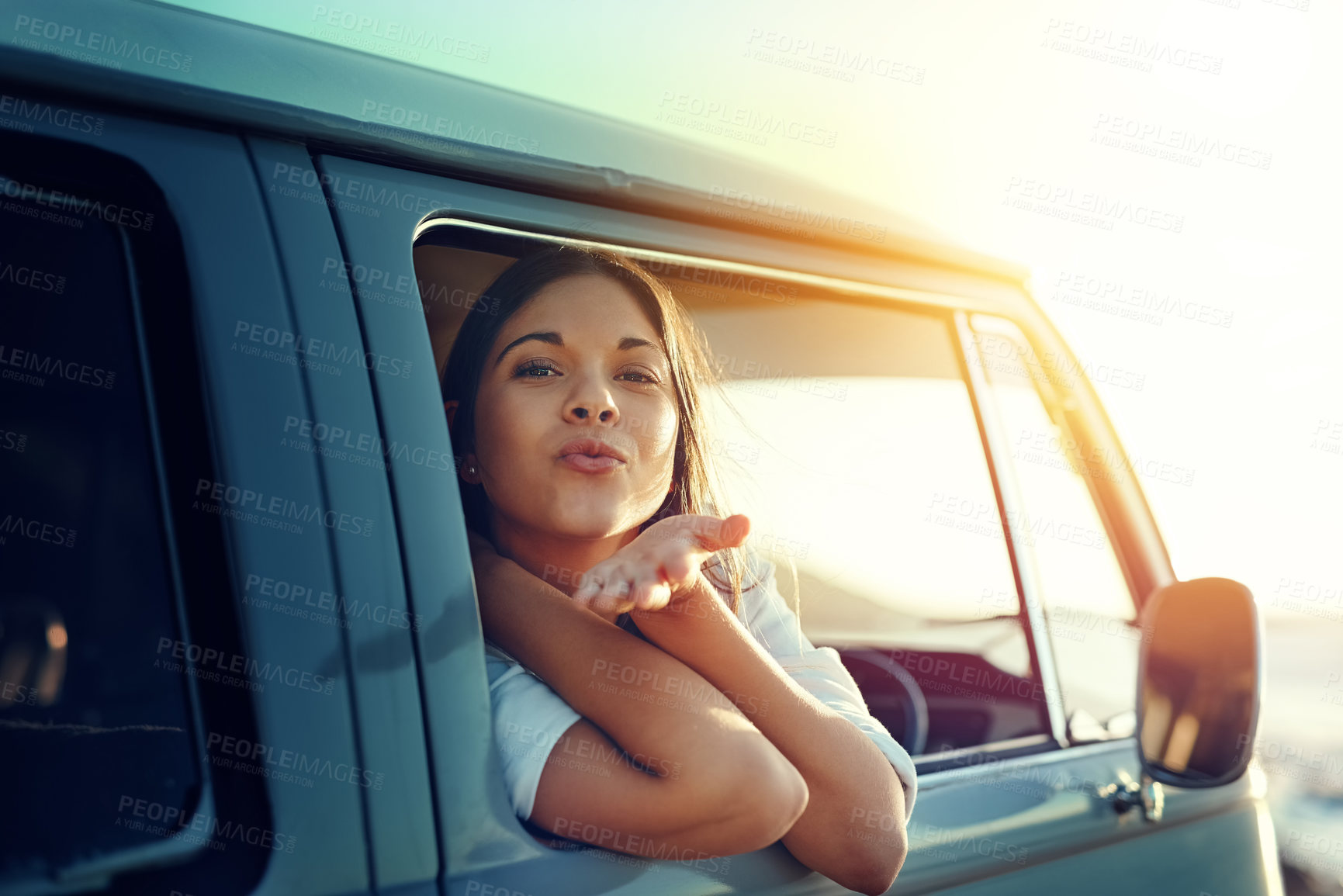 Buy stock photo Shot of a young woman leaning out of a van’s window and blowing a kiss on a roadtrip