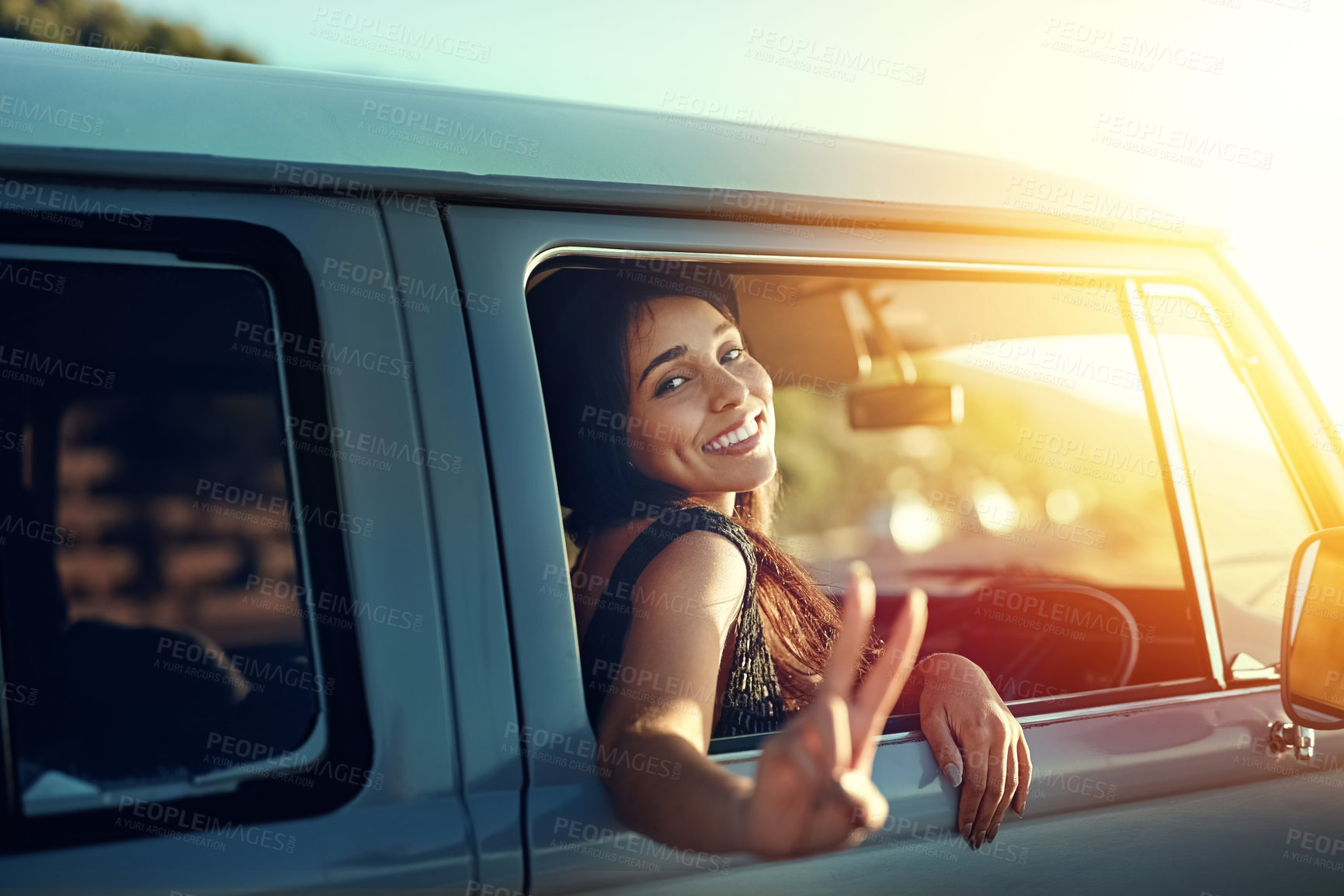 Buy stock photo Shot of a young woman leaning out of a van’s window and showing a peace sign on a roadtrip