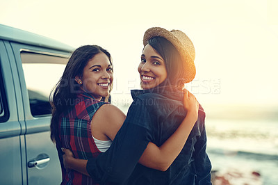 Buy stock photo Shot of two affectionate friends stopping at the beach during their roadtrip