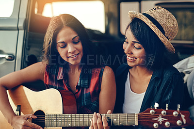 Buy stock photo Shot of a young woman playing a guitar on a road trip with her friend