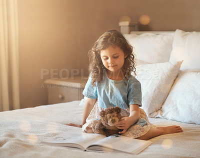 Buy stock photo Shot of an adorable little girl at home reading a storybook on her bed with her teddybear