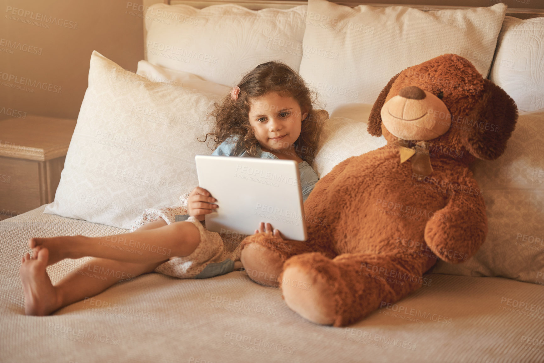 Buy stock photo Girl, child and tablet on bed in home for video, streaming or application for subscription with bear toys. Kid, relax and digital touchscreen in family house for movie, film or cartoon in New Zealand