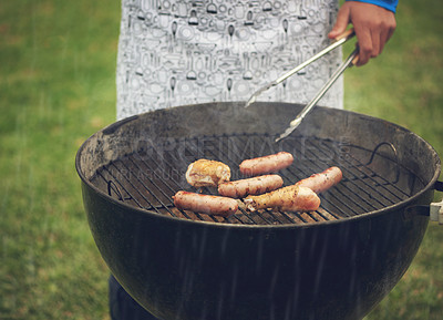 Buy stock photo Unrecognizable shot of a man barbecuing chicken and sausage outside in the rain