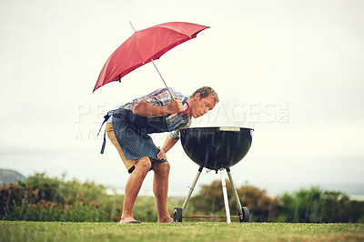 Buy stock photo Umbrella, rain and a man outdoor to barbecue food for cooking or insurance in the winter season. Storm, weather and grill with a male person getting wet while trying to bbq on a grass lawn or garden