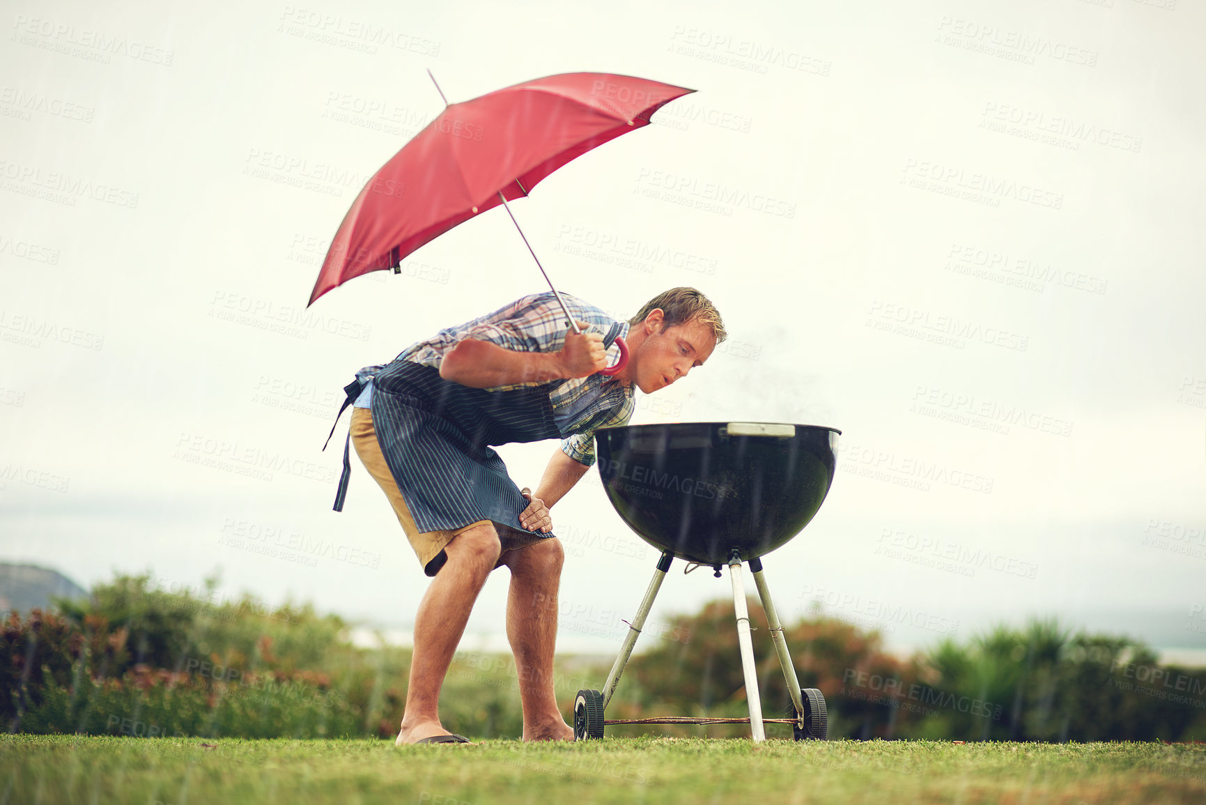 Buy stock photo Umbrella, rain and a man outdoor to barbecue food for cooking or insurance in the winter season. Storm, weather and grill with a male person getting wet while trying to bbq on a grass lawn or garden