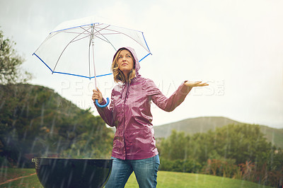 Buy stock photo Shot of a woman having a barbecue outside in the rain while holding an umbrella and looking up into the sky