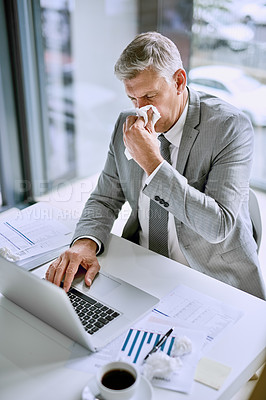 Buy stock photo Cropped shot of an ill businessman blowing his nose in the office while working on a laptop