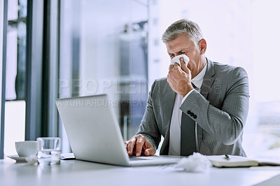 Buy stock photo Cropped shot of a sick businessman blowing his nose and working on a laptop in the office