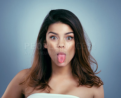 Buy stock photo Studio shot of a beautiful young woman sticking out her tongue against a blue background