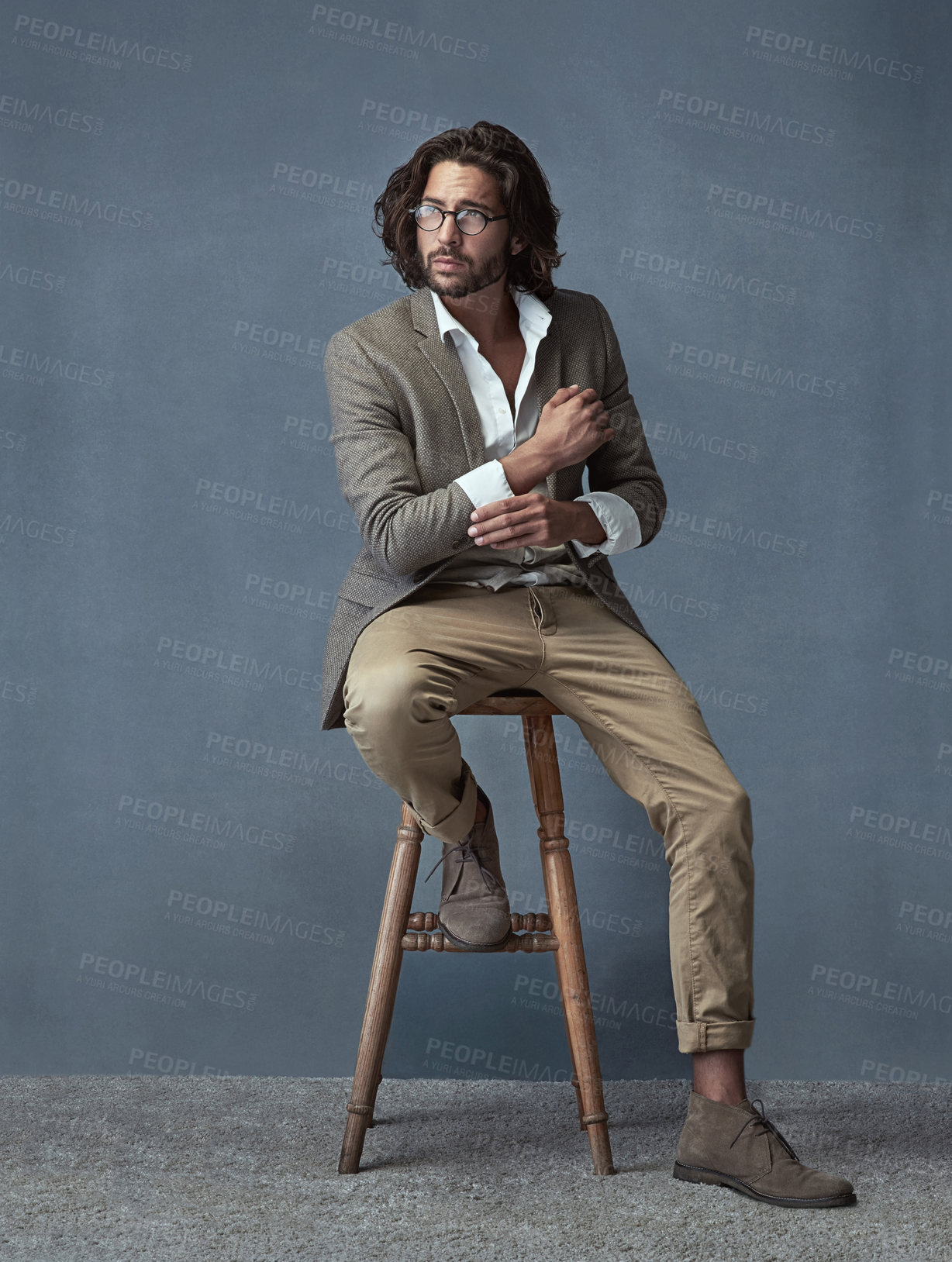 Buy stock photo Full length studio shot of a handsome and stylish young man sitting on a stool against a grey background
