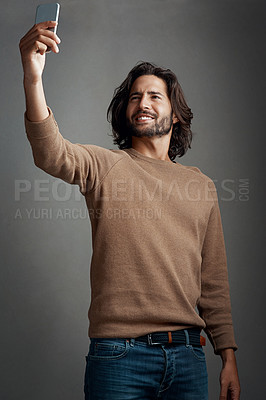 Buy stock photo Studio shot of a handsome young man taking a selfie on his cellphone against a gray background