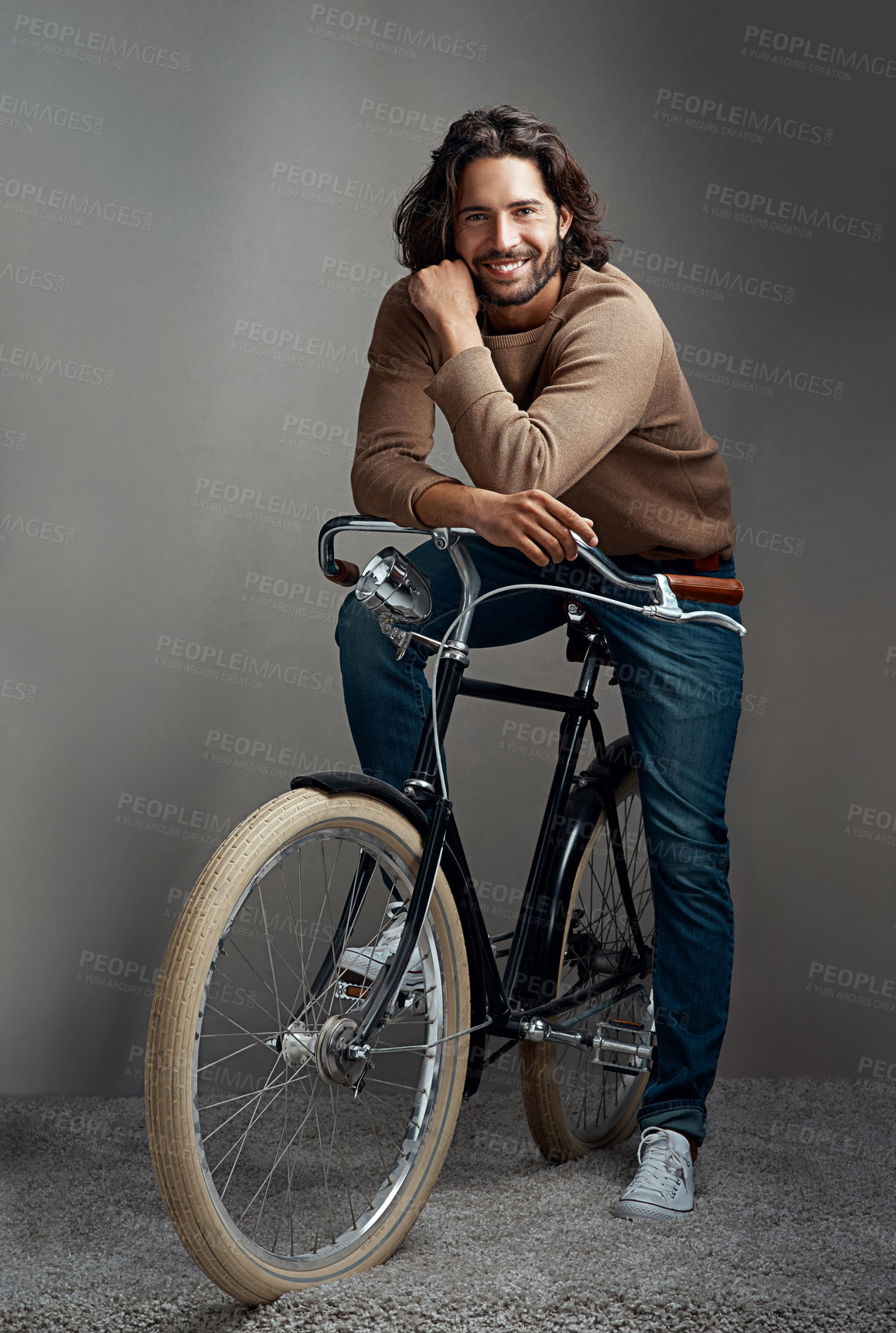 Buy stock photo Studio shot of a handsome young man leaning against a bicycle in front of a gray background