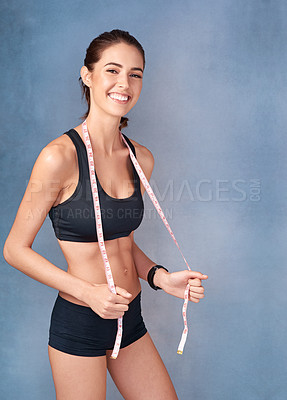Buy stock photo Studio portrait of a sporty young woman posing with a tape measure against a grey background