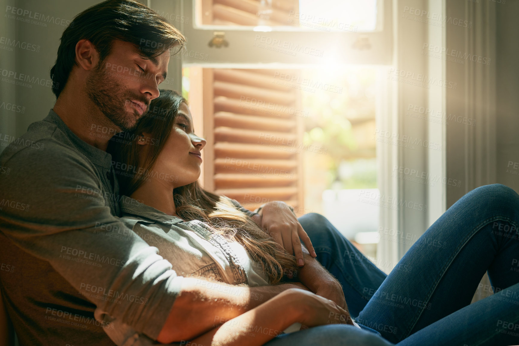 Buy stock photo Shot of an affectionate young couple holding each other at home in the sunlight