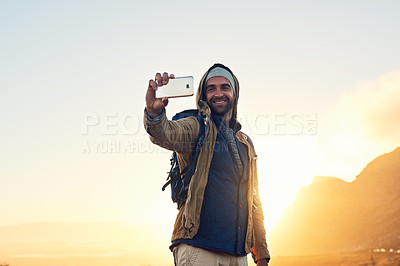 Buy stock photo Shot of a handsome hiker on top of a mountain taking a selfie