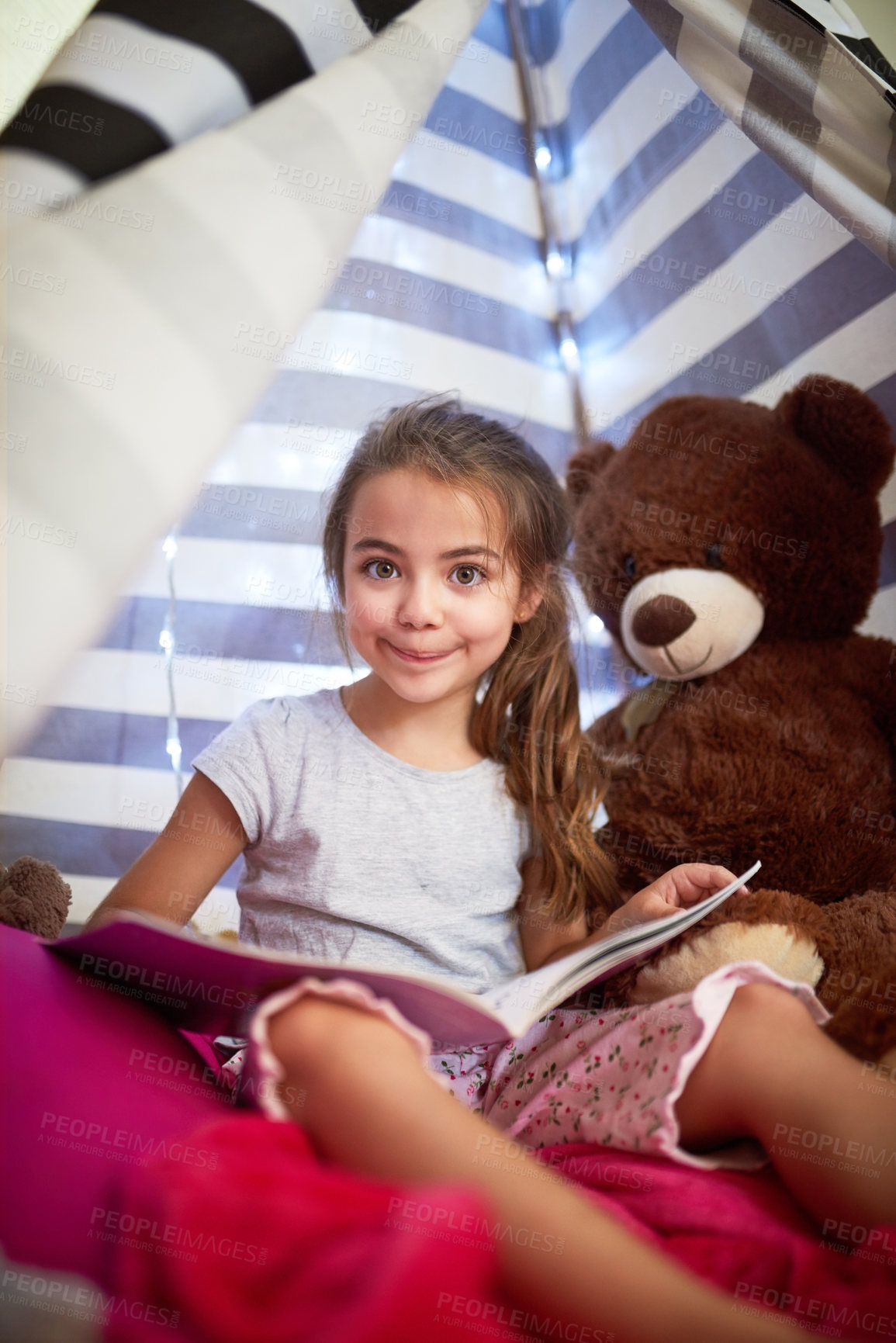 Buy stock photo Portrait of a little girl reading a book with her teddybear in a tent at home