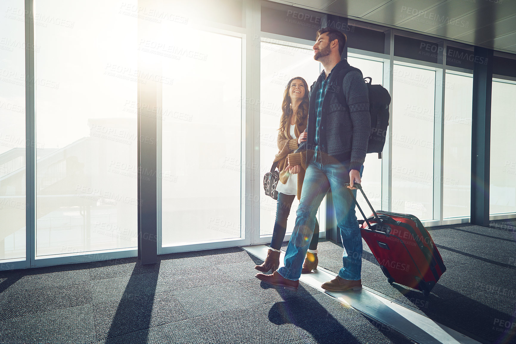 Buy stock photo Shot of a young couple walking together in an airport with their luggage while holding one another