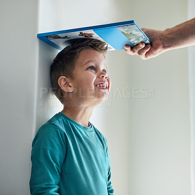 Buy stock photo Cropped shot of a little boy getting his height measured against a wall with a book