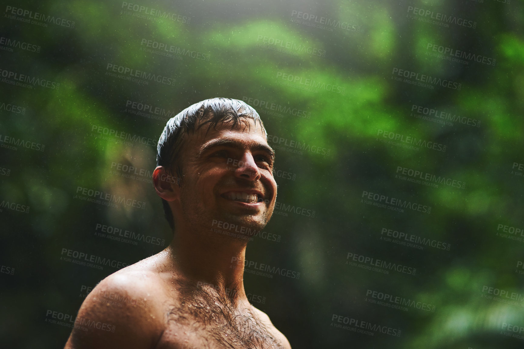 Buy stock photo Shot of a young man being happy in the jungle while covered in water and smiling all the way