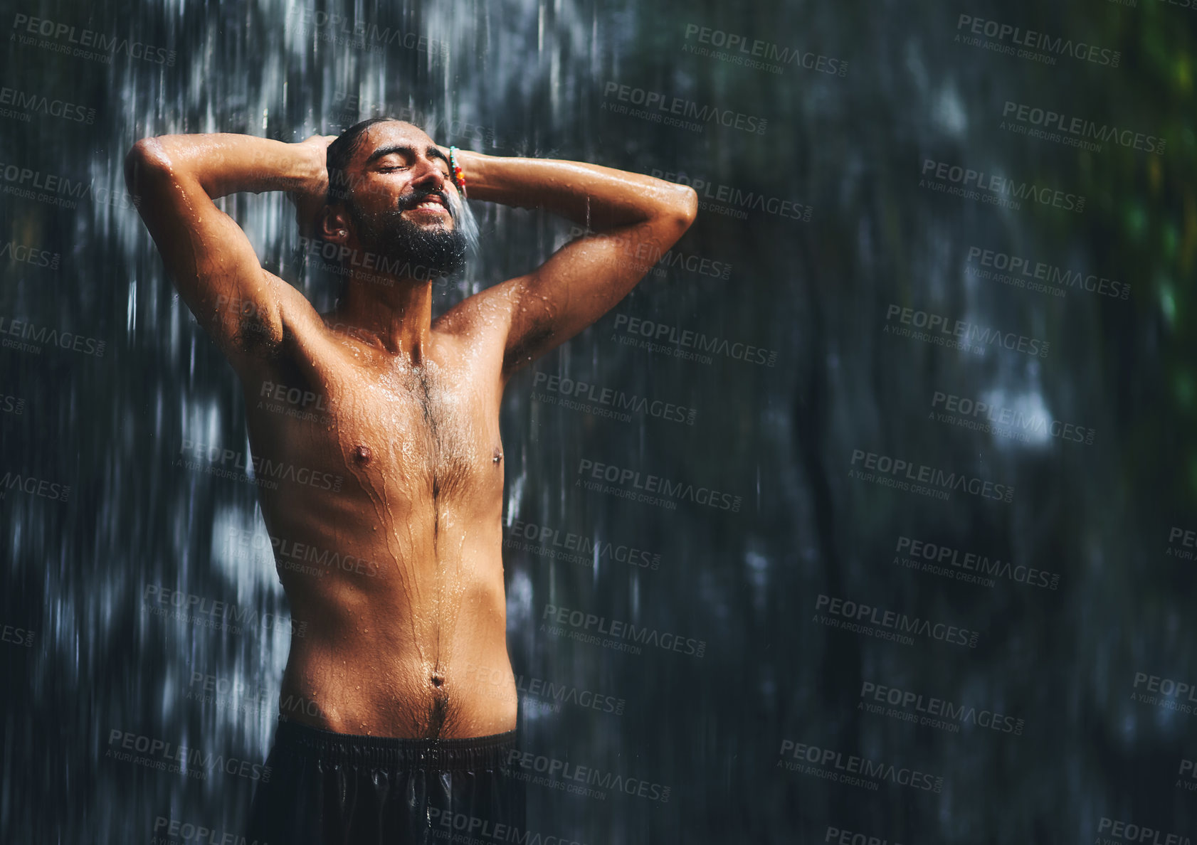 Buy stock photo Shot of a young man standing under a waterfall being completely soaked in water but loving every moment of it