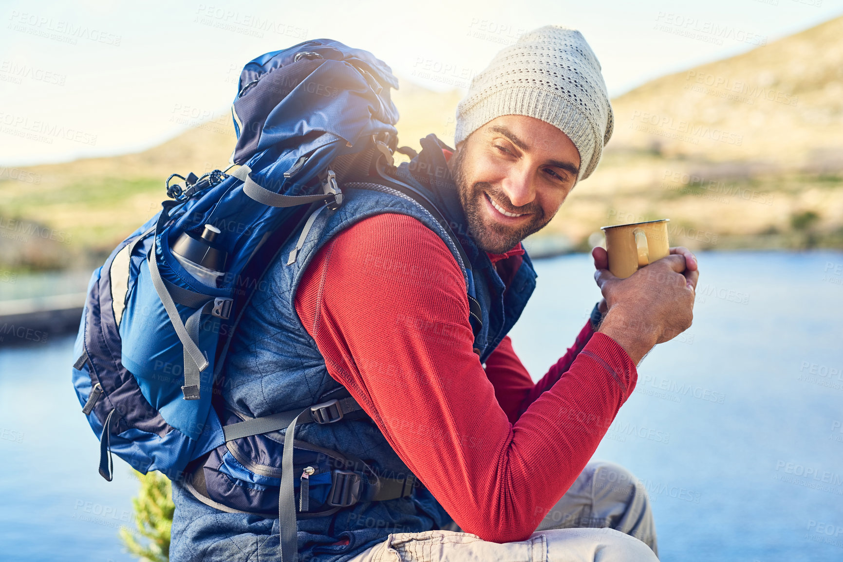 Buy stock photo Shot of a happy hiker drinking coffee while admiring a lake view on a trail