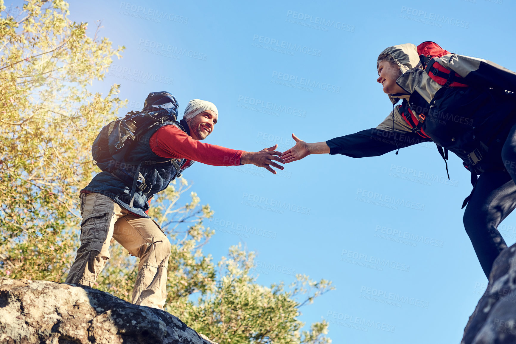 Buy stock photo Shot of a pair of happy hikers reaching for each other's hands on a mountain trail