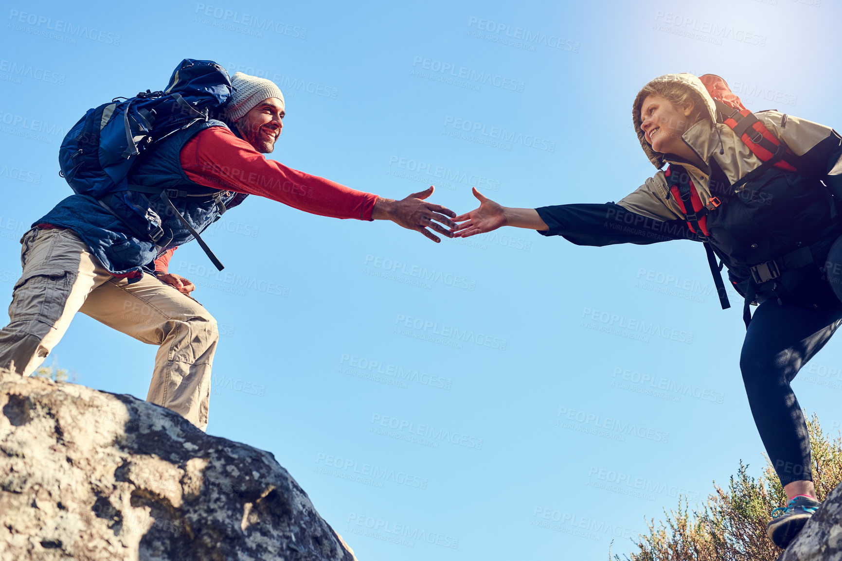 Buy stock photo Shot of a pair of happy hikers reaching for each other's hands on a mountain trail