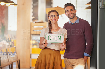 Buy stock photo Portrait of two young business owners standing in the doorway of their coffee shop with an open sign