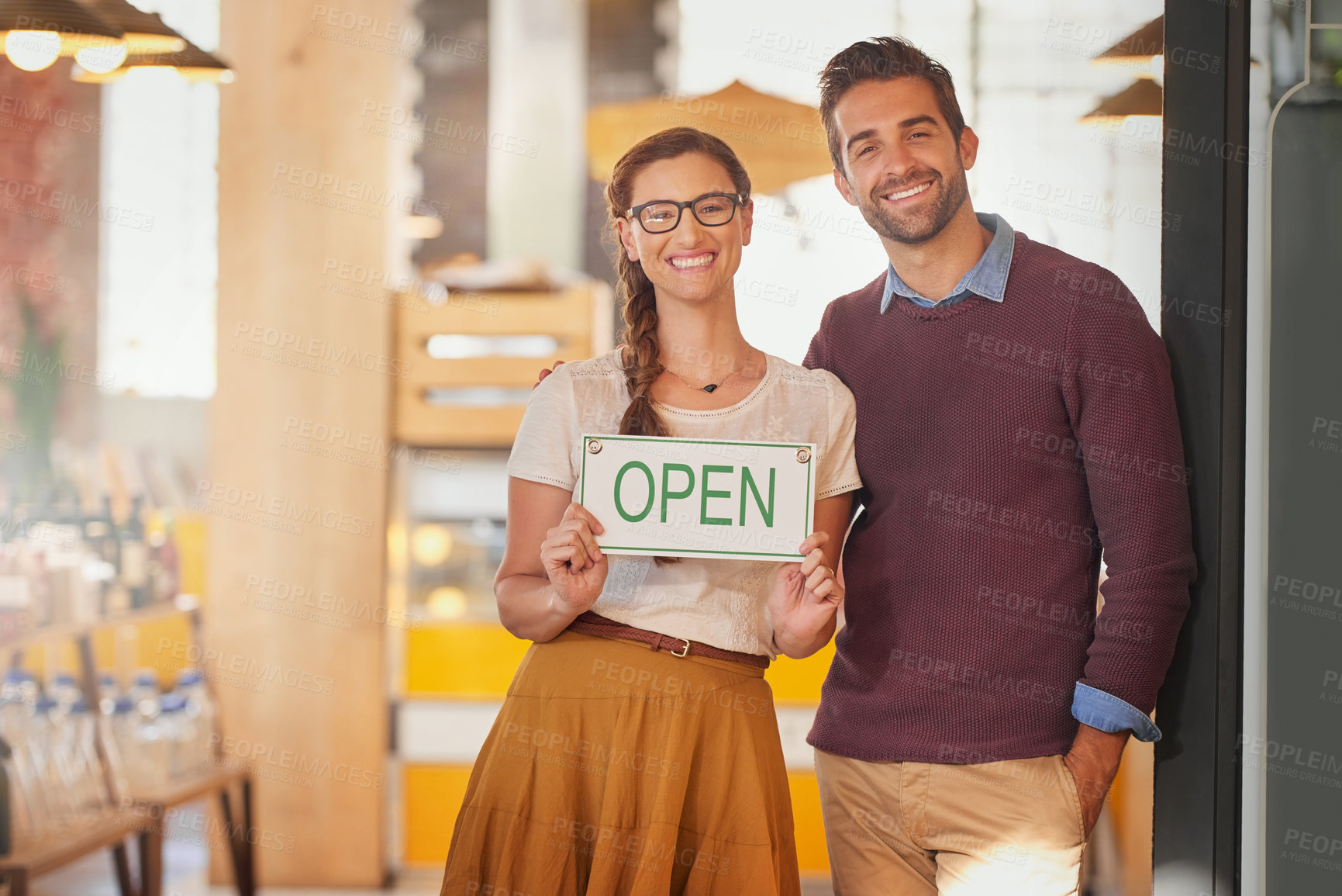 Buy stock photo Portrait of two young business owners standing in the doorway of their coffee shop with an open sign