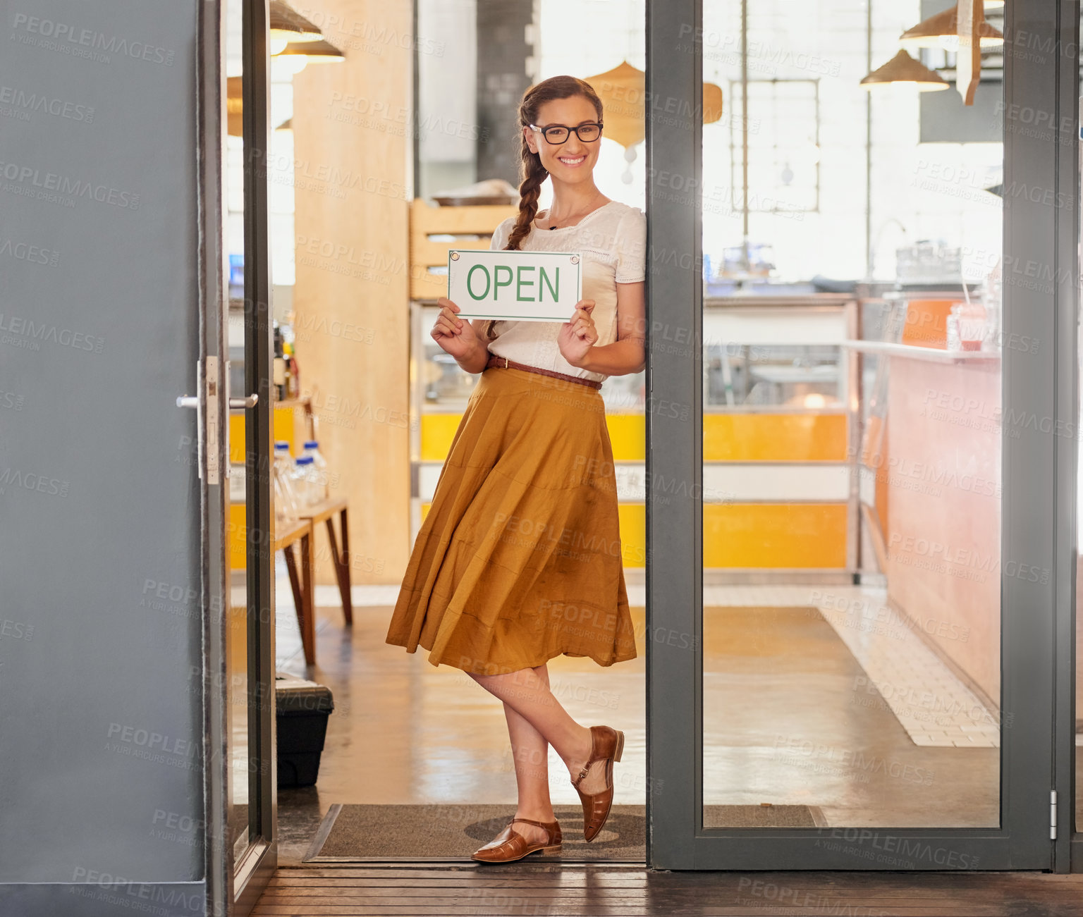Buy stock photo Portrait of a young business owner standing in the doorway of her coffee shop with an open sign
