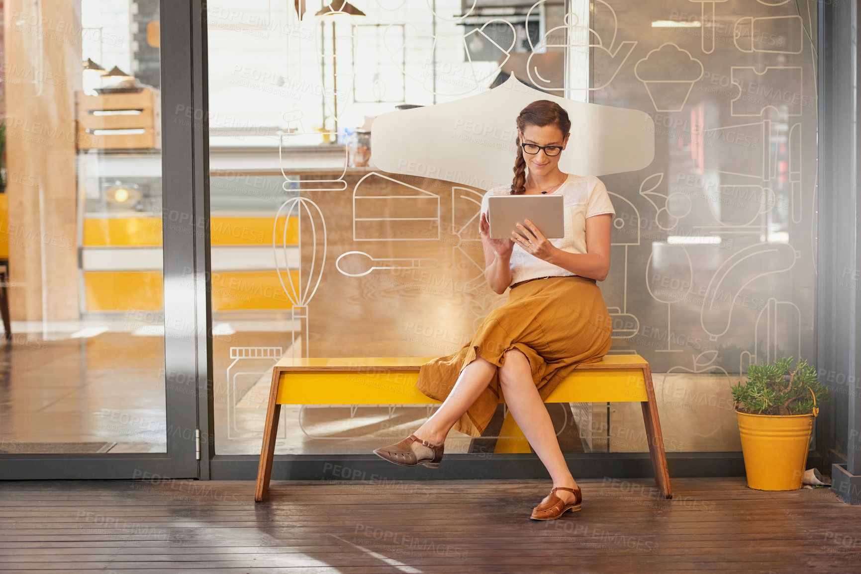 Buy stock photo Shot of a happy young woman using her tablet while sitting on a bench outside a coffee shop