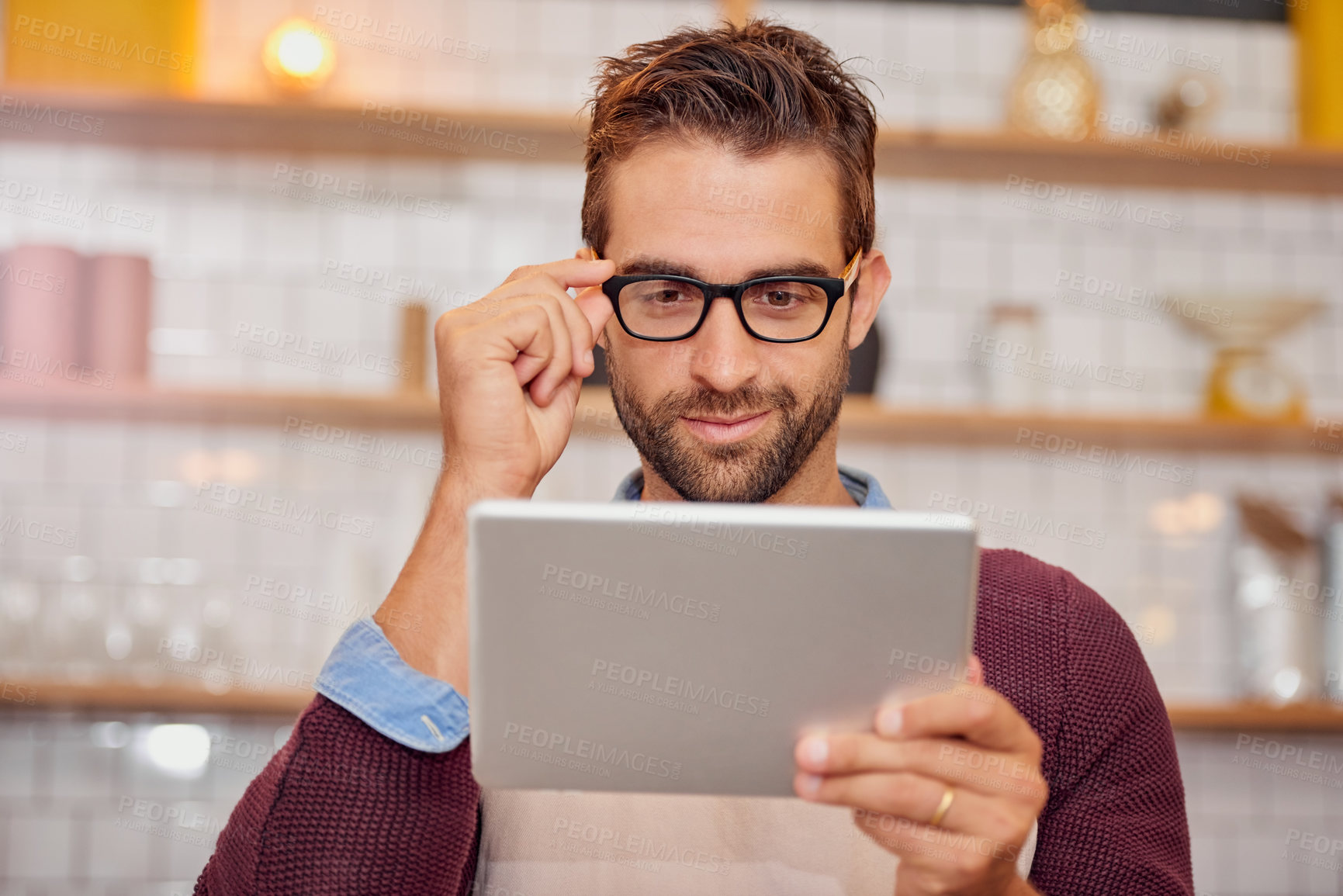 Buy stock photo Shot of happy young business owner using a tablet while standing in his coffee shop