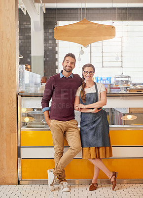 Buy stock photo Portrait of two young business owners posing in front of the counter in their coffee shop