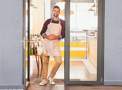 Buy stock photo Portrait of a young business owner standing in the doorway of his coffee shop with an apron on