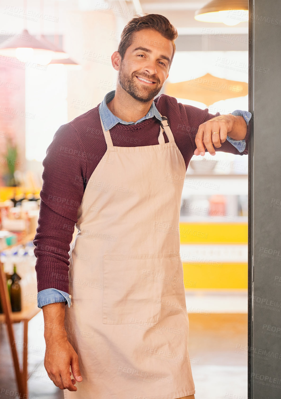 Buy stock photo Portrait of a young business owner standing in the doorway of his coffee shop with an apron on